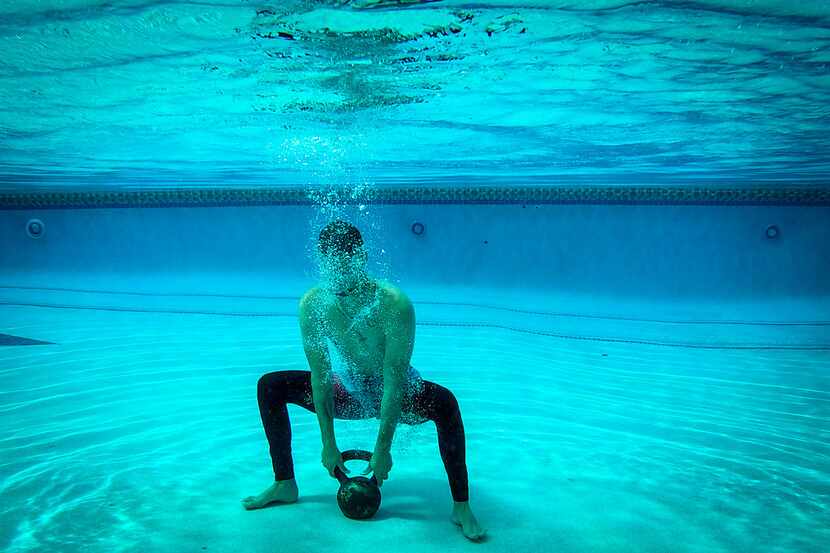 Texas Rangers pitcher Alex Claudio does squats underwater while holding a kettlebell during...
