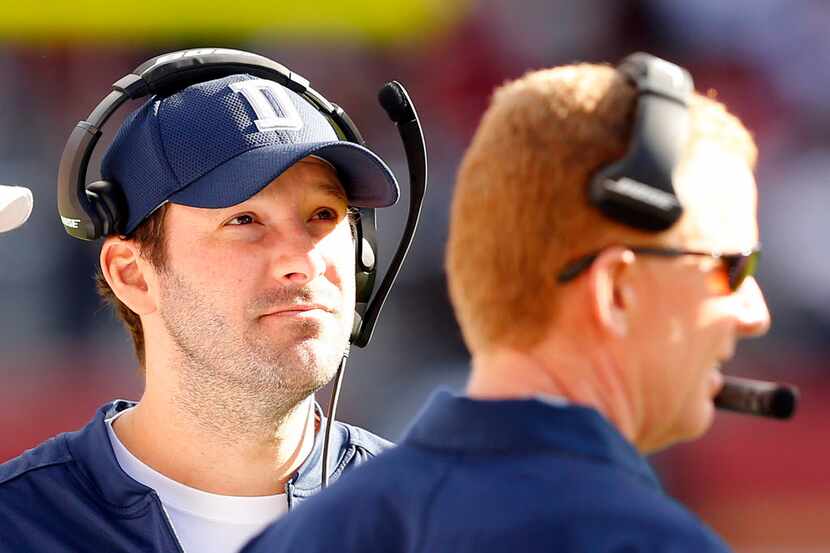 Dallas Cowboys quarterback Tony Romo (left) follwos the game on the headset with head coach...