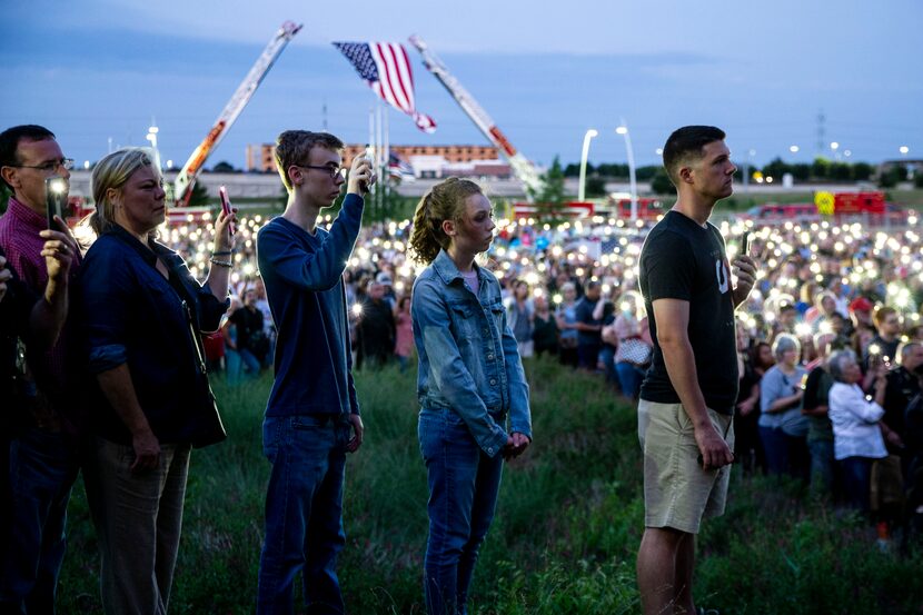 Mourners hold aloft cellphone flashlights after high winds blew out candles during a vigil...