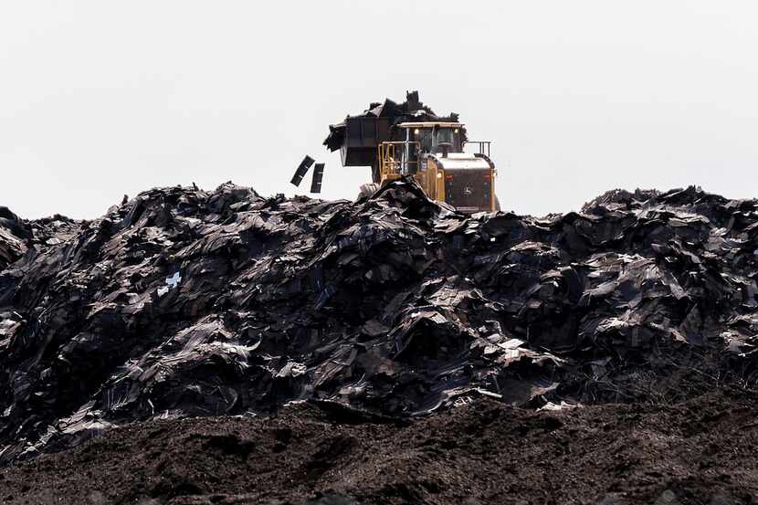 Heavy equipment works atop the mountain of roofing shingles at Blue Star Recycling that...