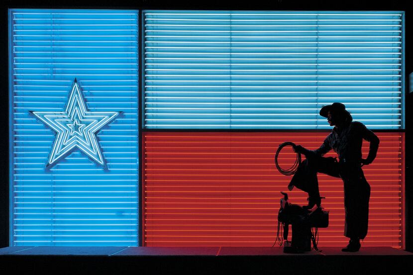 A cowboy poses in front of a large neon interpretation of the Texas flag at the Institute of...