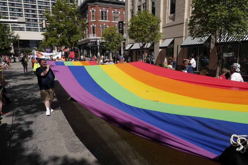 Members of HELP (Health Education Learning Project) march a rainbow flag down Houston St. at...