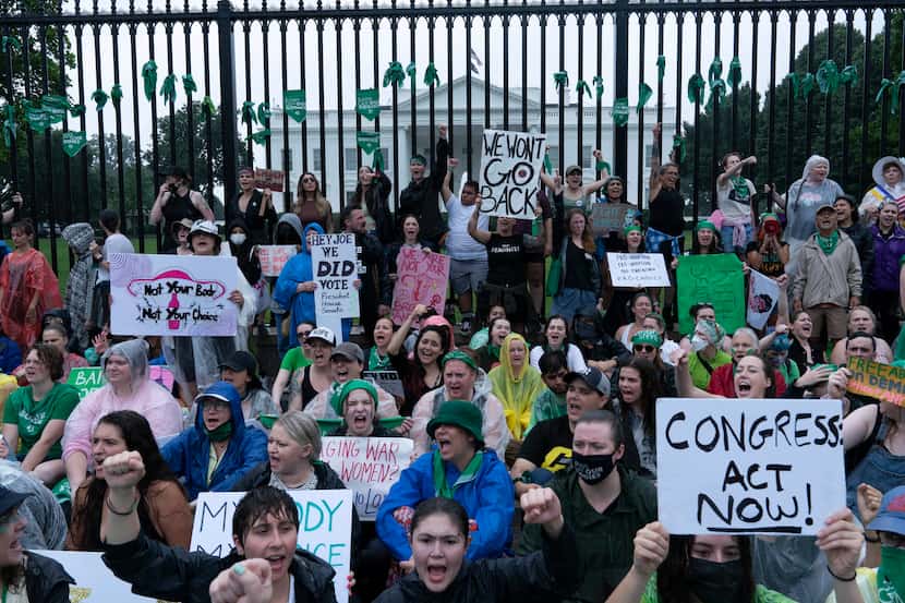 Abortion-rights demonstrators shout slogans after tying green flags to the fence of the...