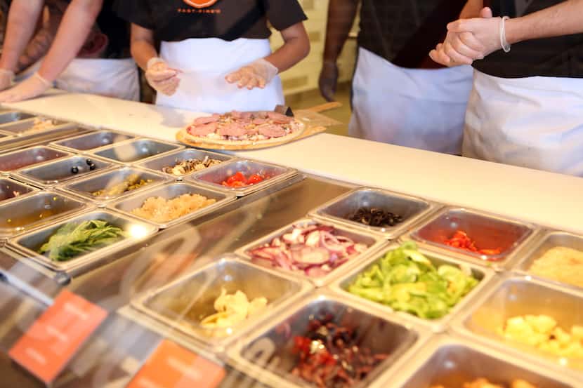 Customers pick their toppings at Blaze Pizza before pizzas are cooked quickly in a very hot...