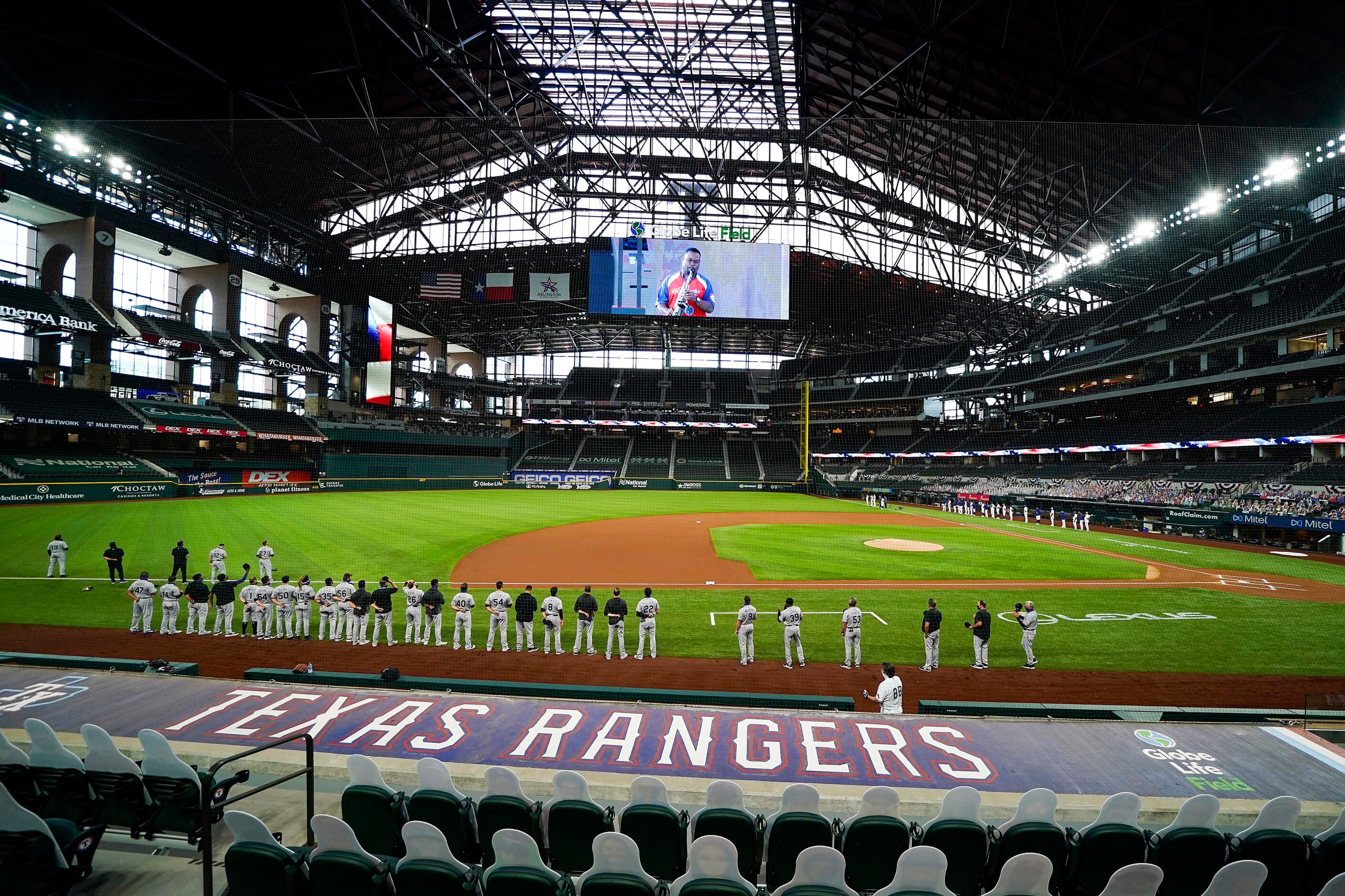 Colorado Rockies (foreground) and Texas Rangers players stand for the national anthem before...