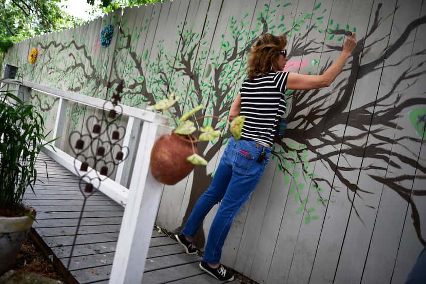 Julie Shipp, who teaches art at Collin College, volunteered to paint a tree mural on a fence...