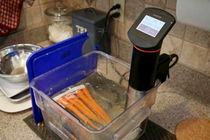 
An immersion circulator (right) heats a vacuum-sealed bag of carrots in a tub of water as...