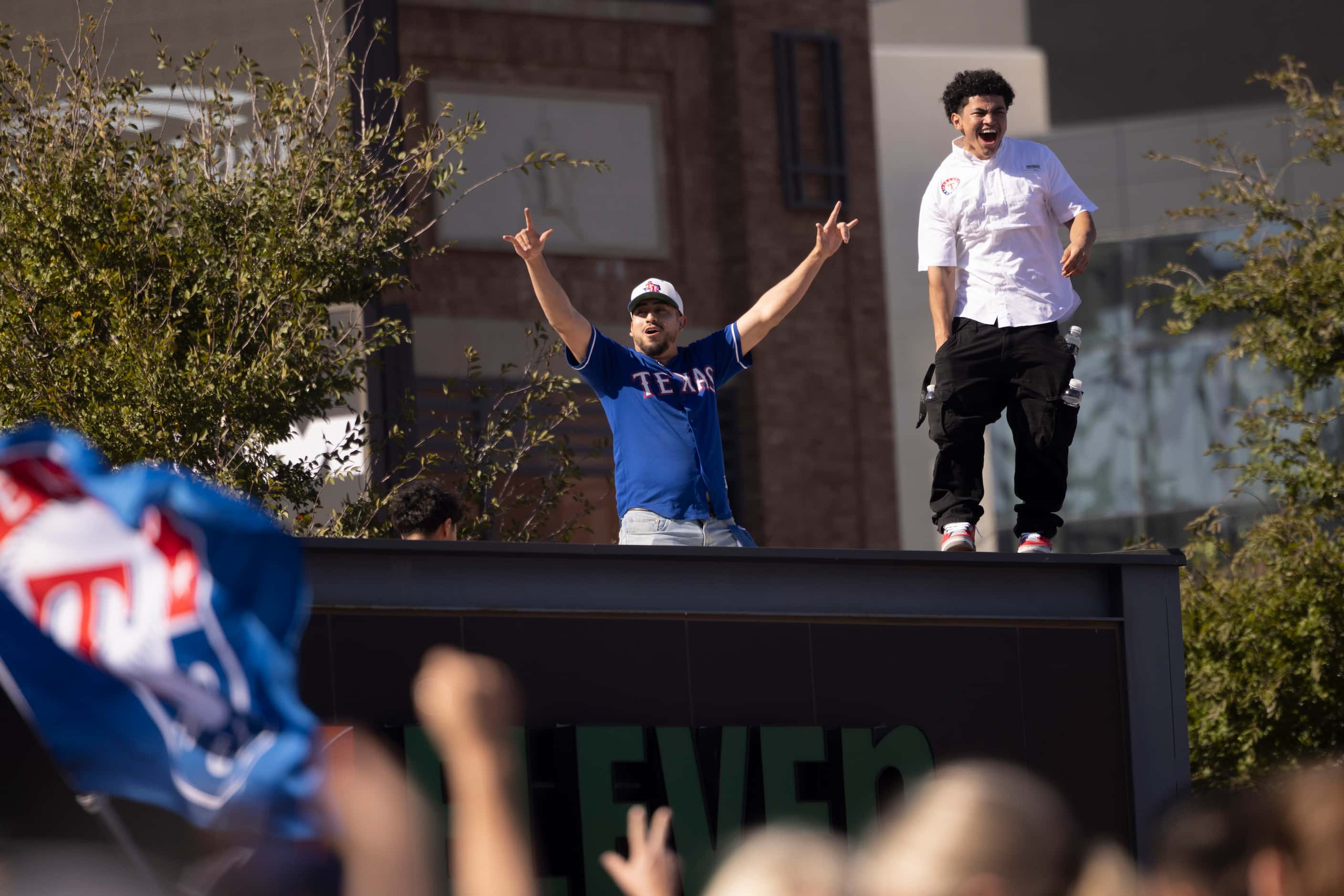 Texas Rangers fans cheer after scaling to the roof of the 7-Eleven outside of Globe Life...