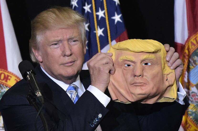 Republican presidential nominee Donald Trump holds a mask of himself which he picked up from...