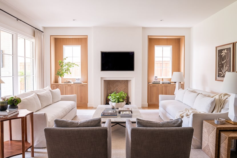 Formal living space outfitted in netural shades, with windows flanking a fireplace