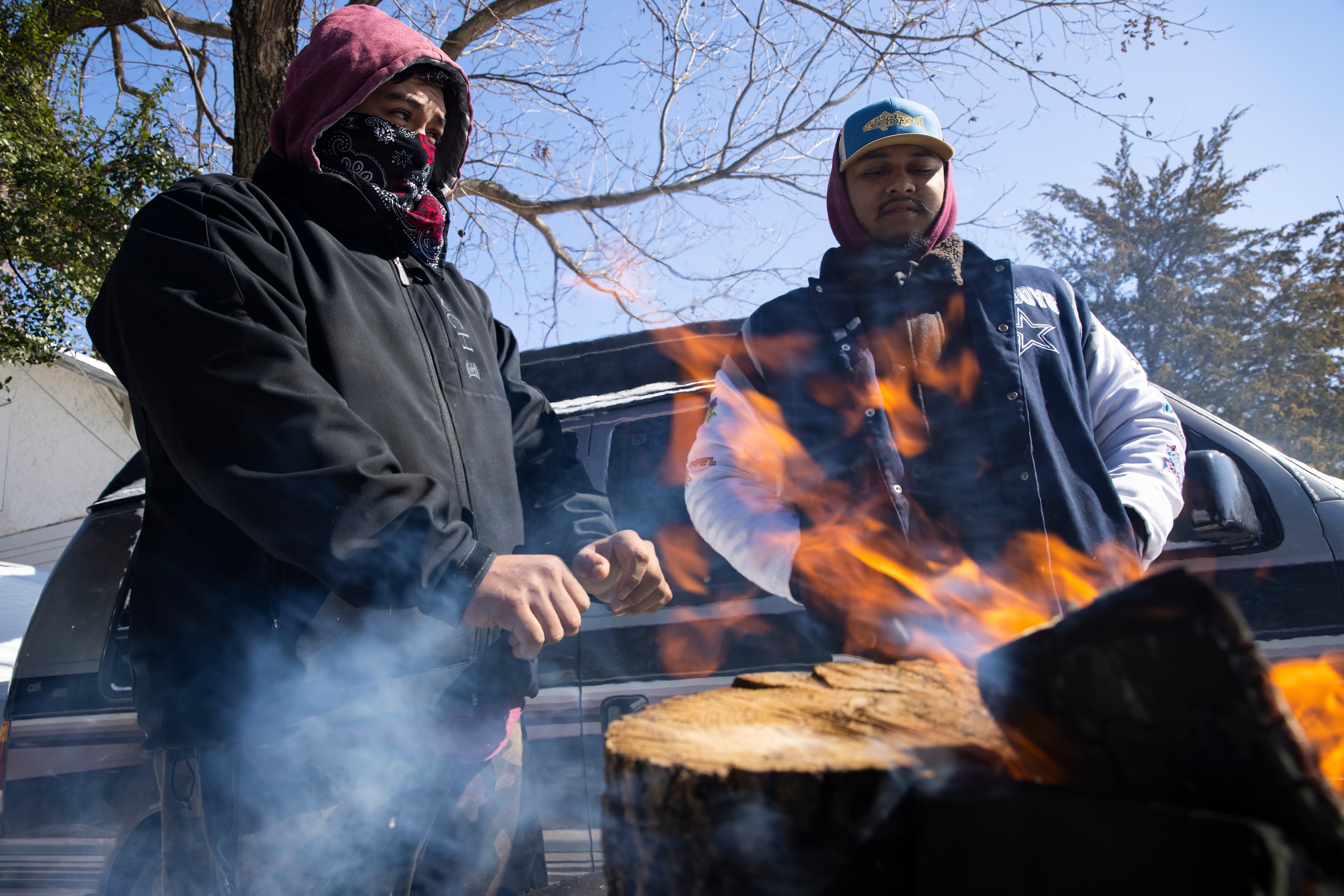 (From left) brothers Alfredo Colon and Eduardo Colon chat over a fire in front of their East...