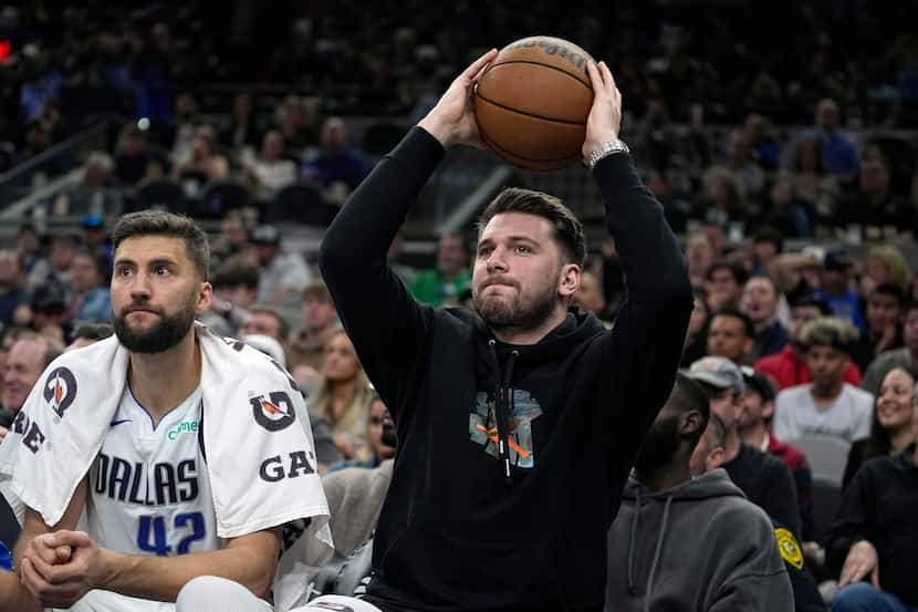 Dallas Mavericks guard Luka Doncic, right, returns the ball to play as he sits on the bench...