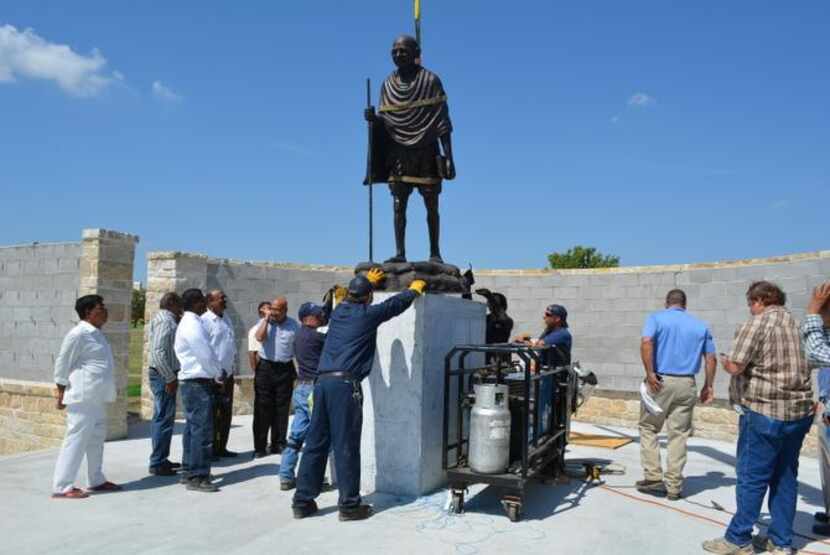 
A construction crew  lowers a bronze statue of Mahatma Gandhi onto a pedestal as a memorial...