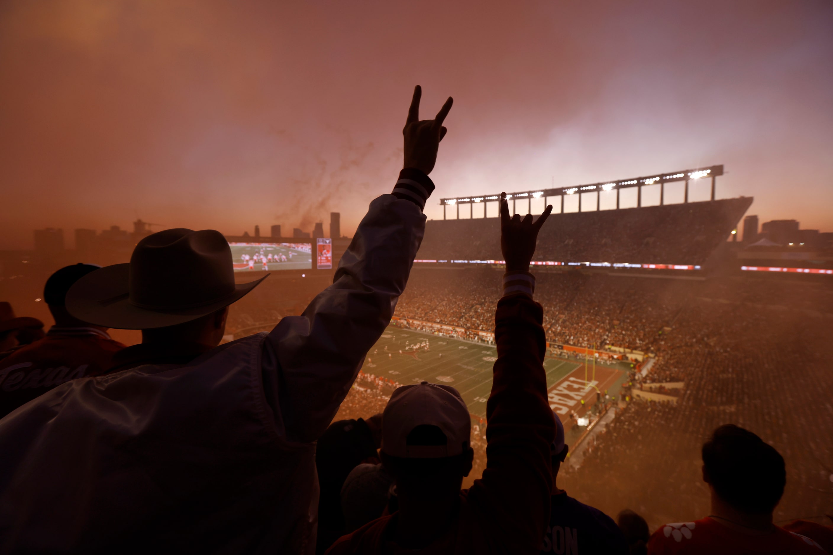 At sunset, Texas Longhorns fans raises their horns as orange smoke fills the stands...