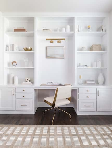 White built-in wall bookshelves around a home workspace, filled with decor, and books, with...