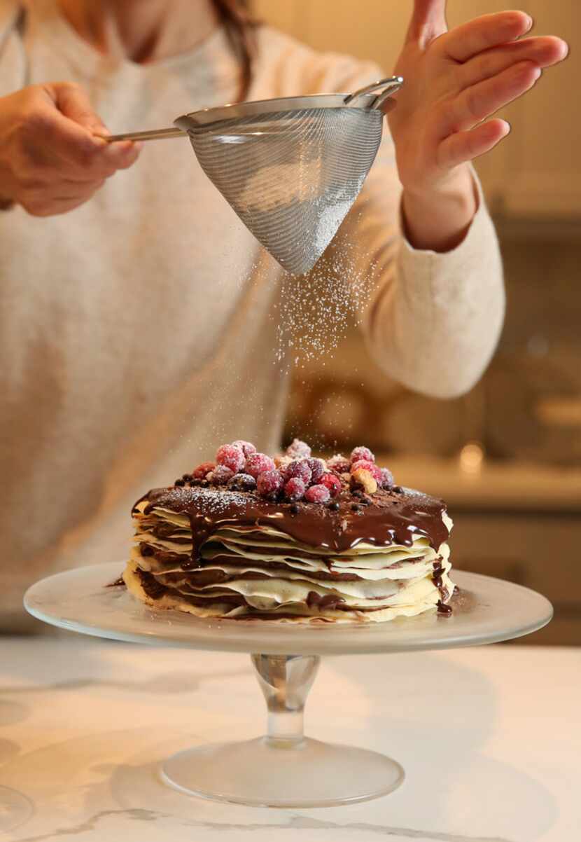 Kristen Massad sprinkles powdered sugar over a Chocolate Hazelnut Crepe Cake