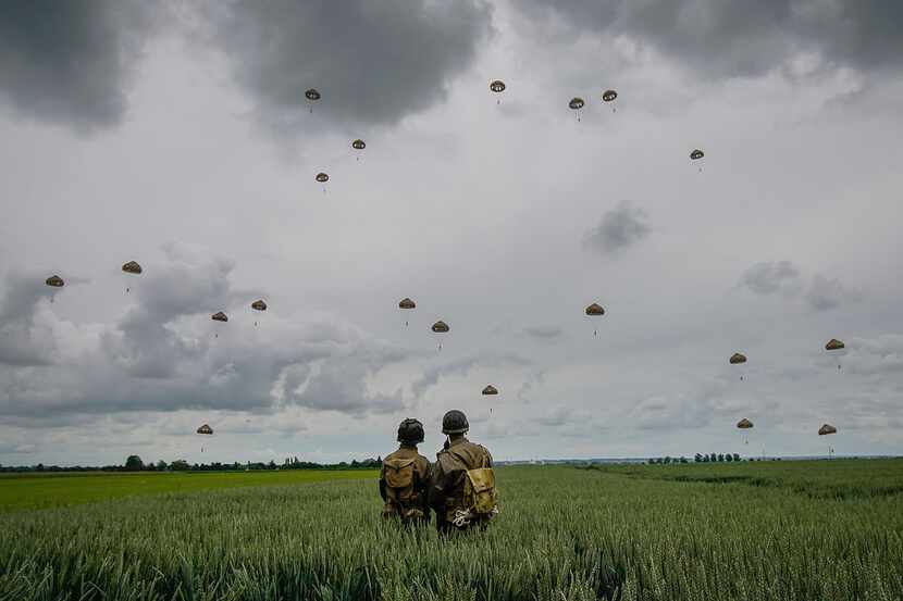 Military re-enactors look on as 280 paratroopers take part in a parachute drop onto fields...