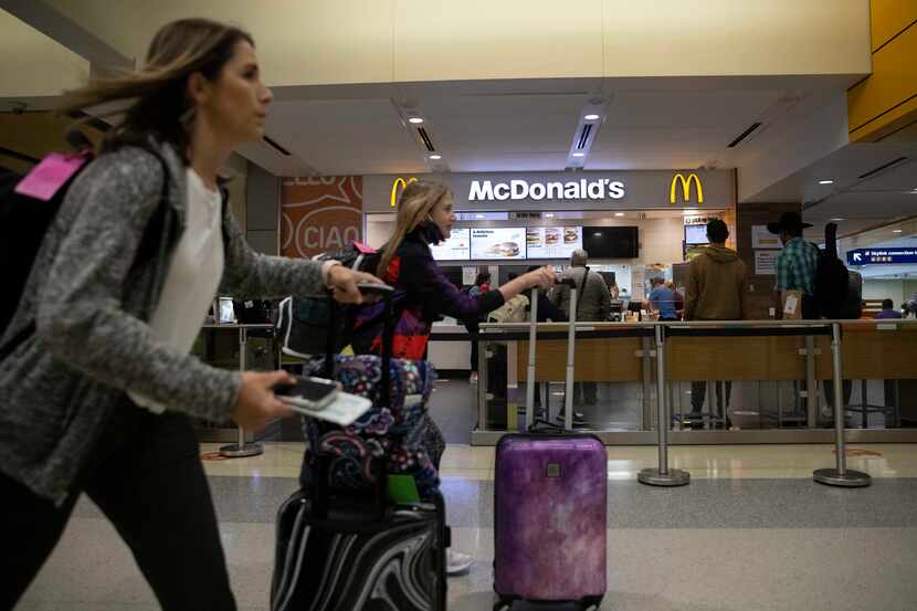 Travelers walk past the McDonald’s in Terminal B at DFW Airport. Airlines are lining up...