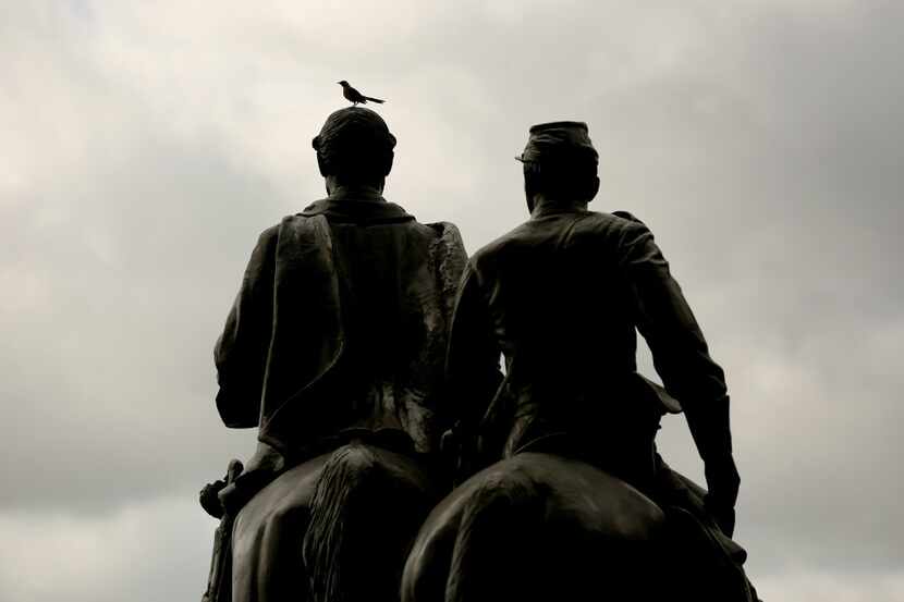 A bird sits atop a statue of Confederate Gen. Robert E. Lee in mid-August, before the statue...