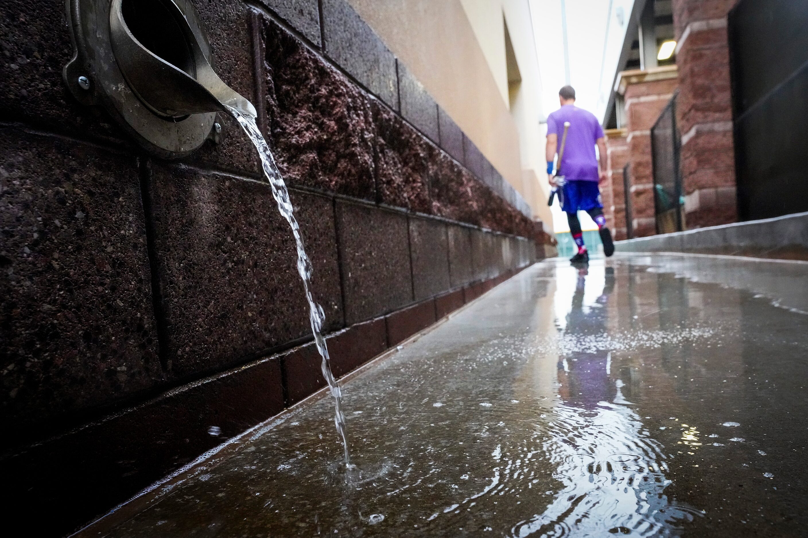 Rain puddles on a walkway as a Texas Rangers player heads to the clubhouse from the indoor...