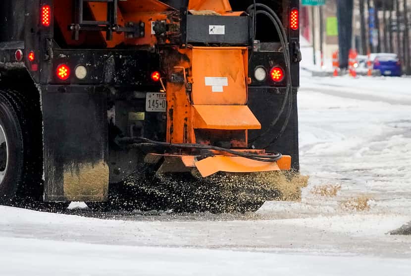 Camiones de la ciudad tiran sal y arena sobre el hielo acumulado en South Akard Street el...