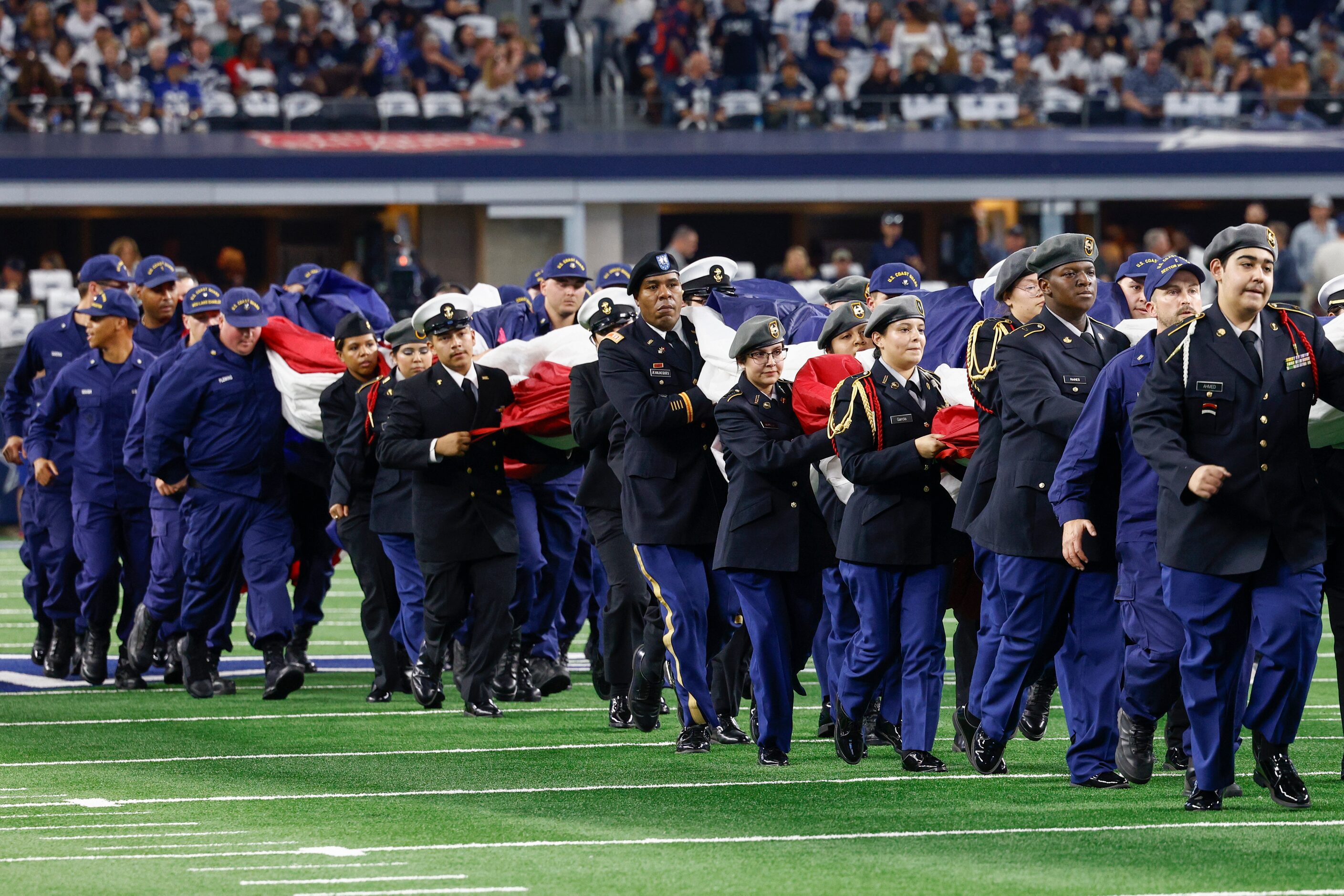 Servicemen and women carry a large American flag off the field after the national anthem...