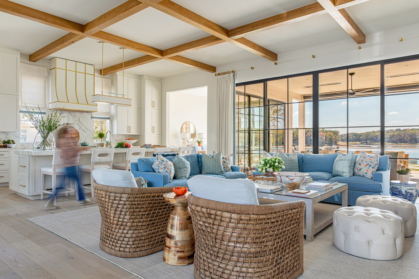 Living room with blue sofas, white ottomans and wicker chairs, next to a white kitchen and...