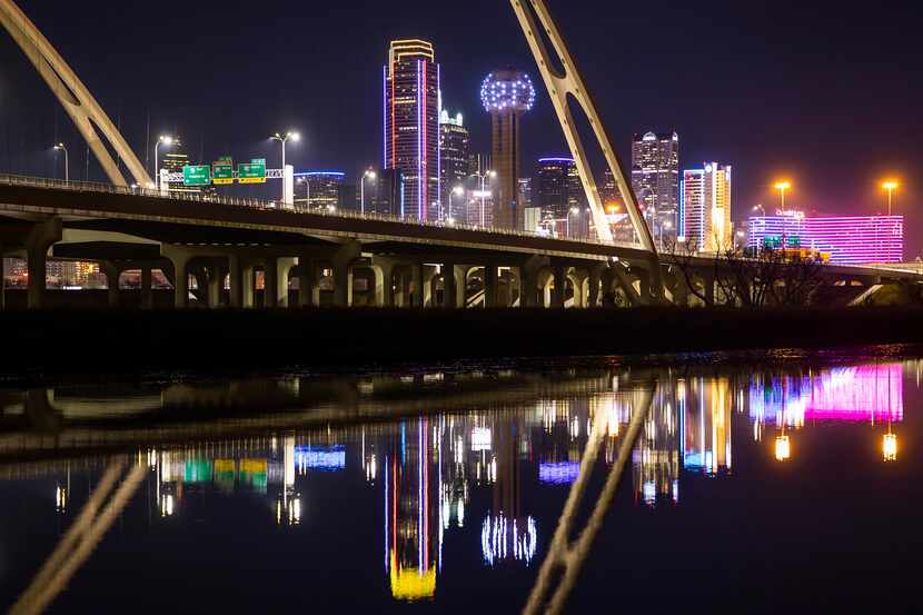 The downtown Dallas skyline glows behind the Margaret McDermott Bridge over the Trinity River.