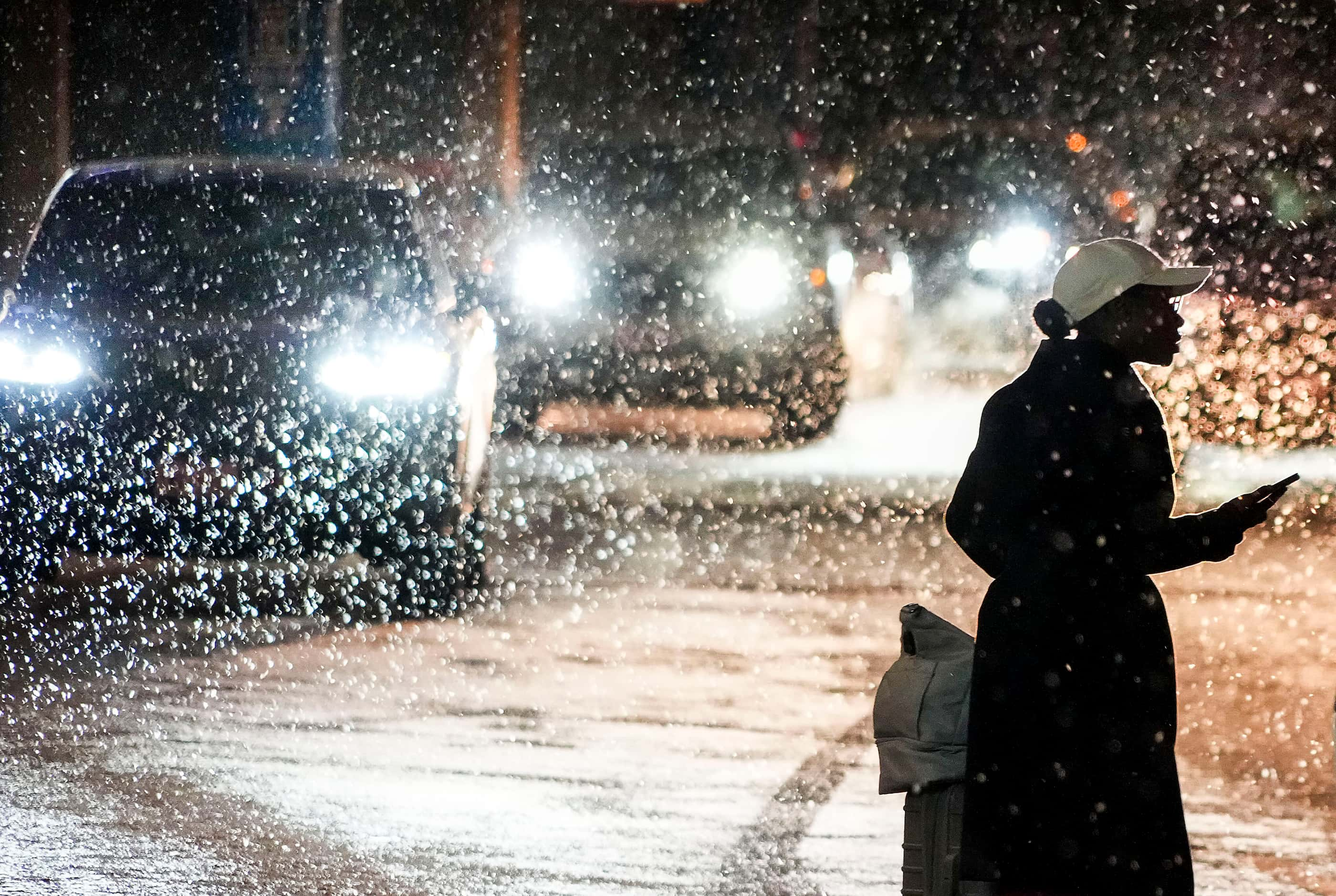 A passenger looks for their ride as snow falls over cars lined up for passenger pickup at ...