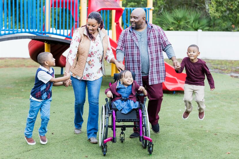 A family with children, one of whom is in wheelchair, walking in a park.