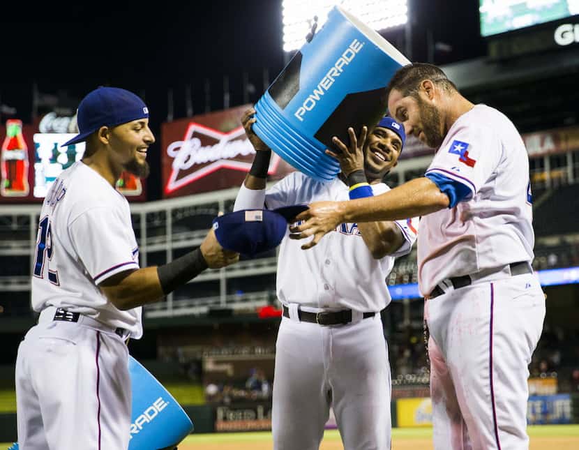 Colby Lewis hands his hat to Rougned Odor so Elvis Andrus can pour water on his head after...