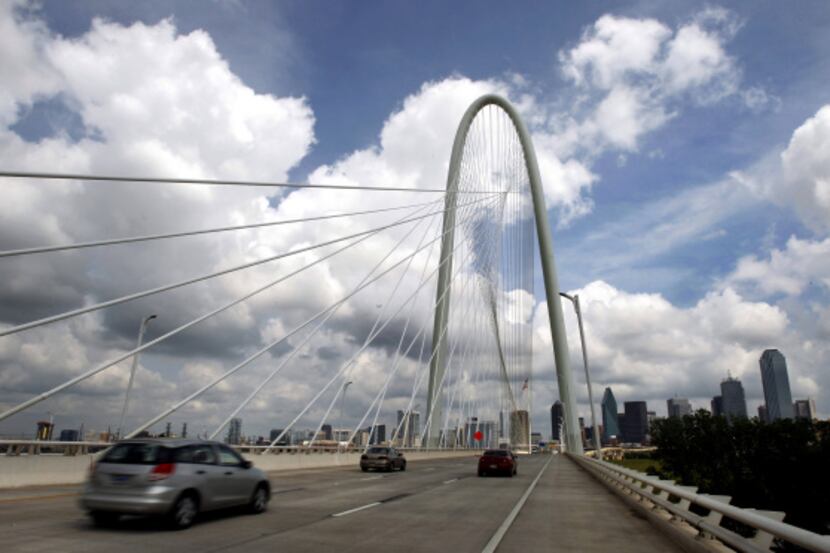 Under splotches of clouds, a soaring arch and a web of cables, the first eastbound traffic...