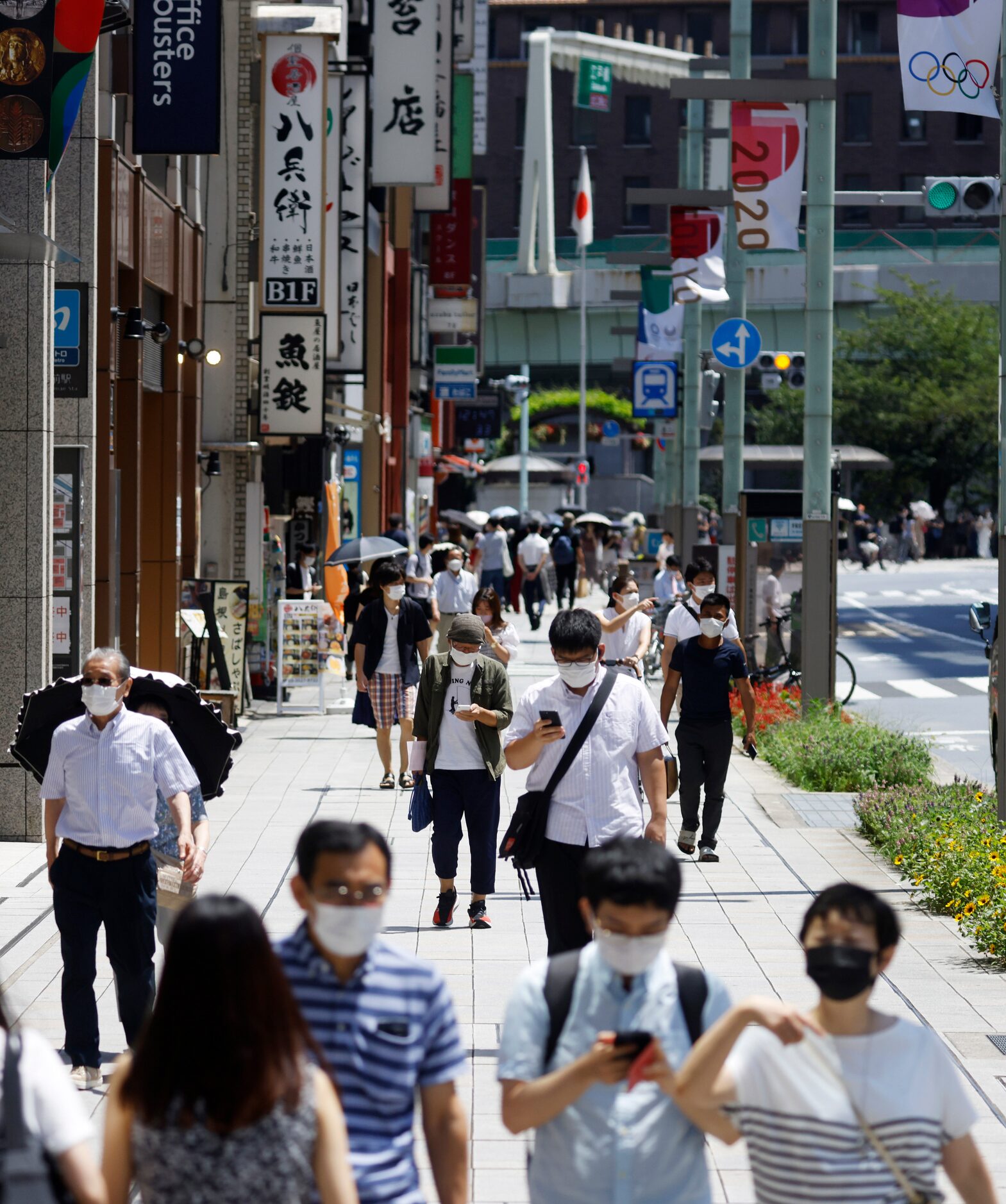 People with masks walk on the sidewalk during the postponed 2020 Tokyo Olympics on Friday,...