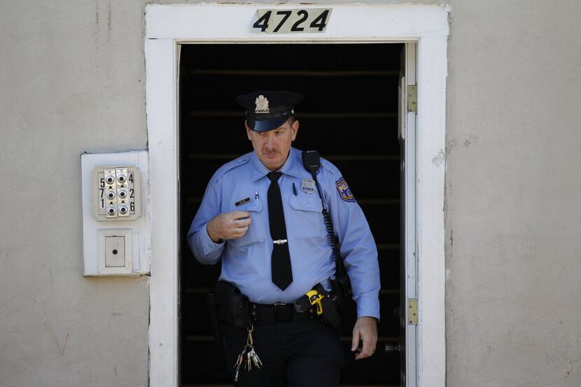 A policeman exits the front doorway of an apartment building.