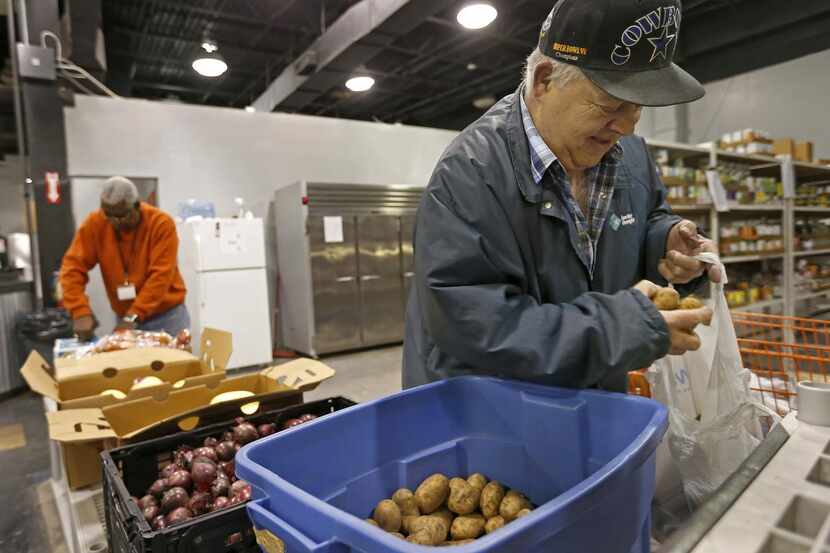 
Herb West bags up potatoes as volunteer Robert Gilliam (background) unpacks groceries at...