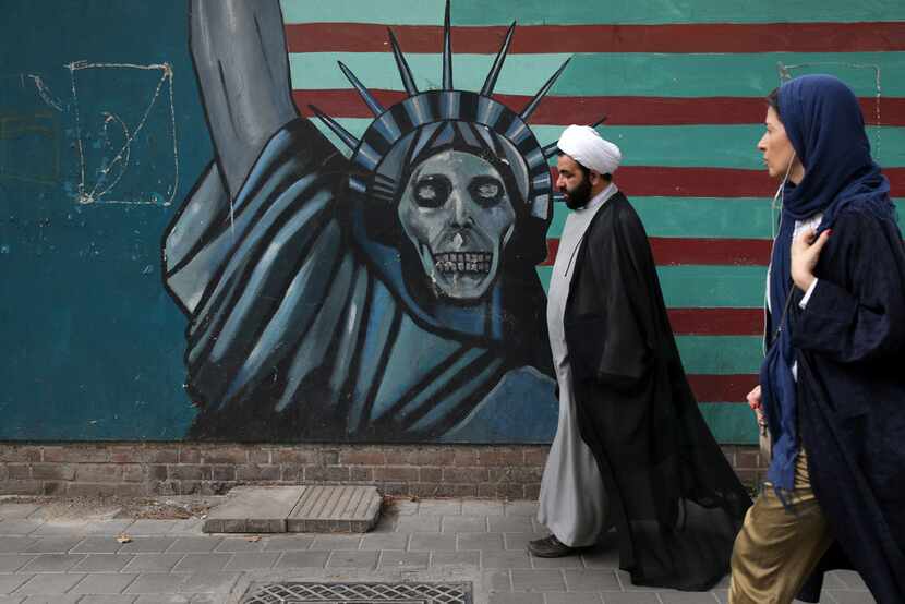 A cleric and a woman walk past an anti-U.S. mural painted on the wall of the former U.S....