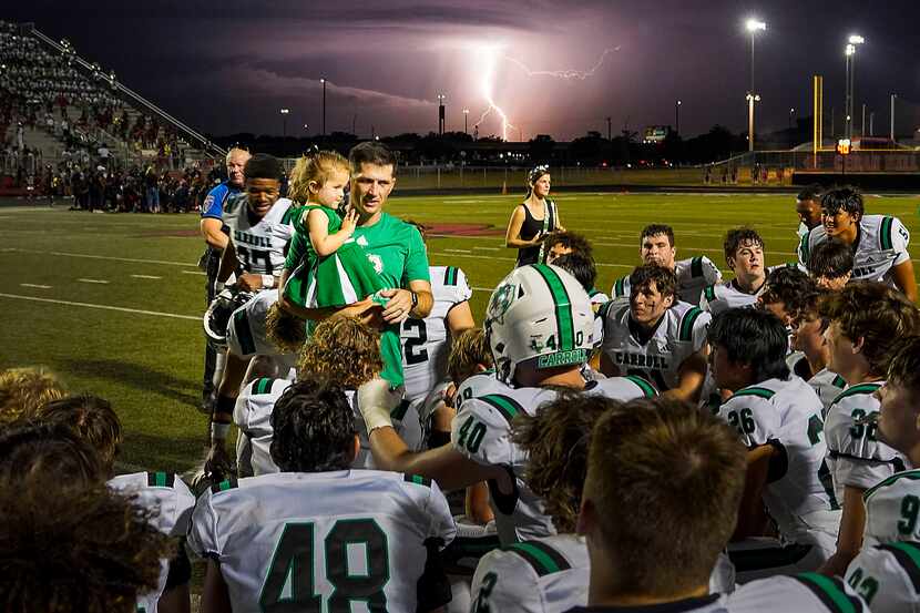 Lightning  is seen in the distance as Southlake Carroll head coach Riley Dodge talks to his...