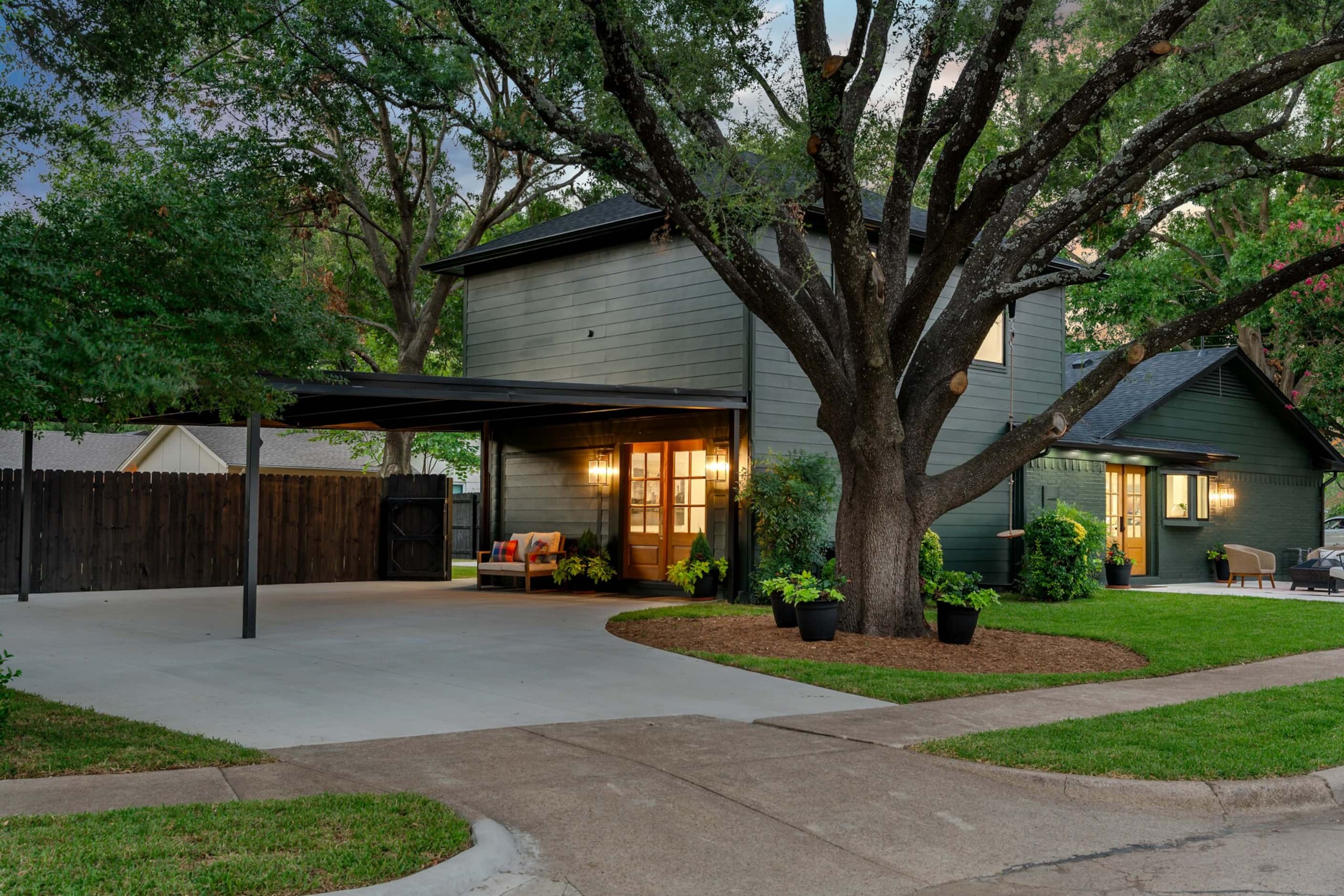 House with dark green exterior, covered carport, large tree in side yard