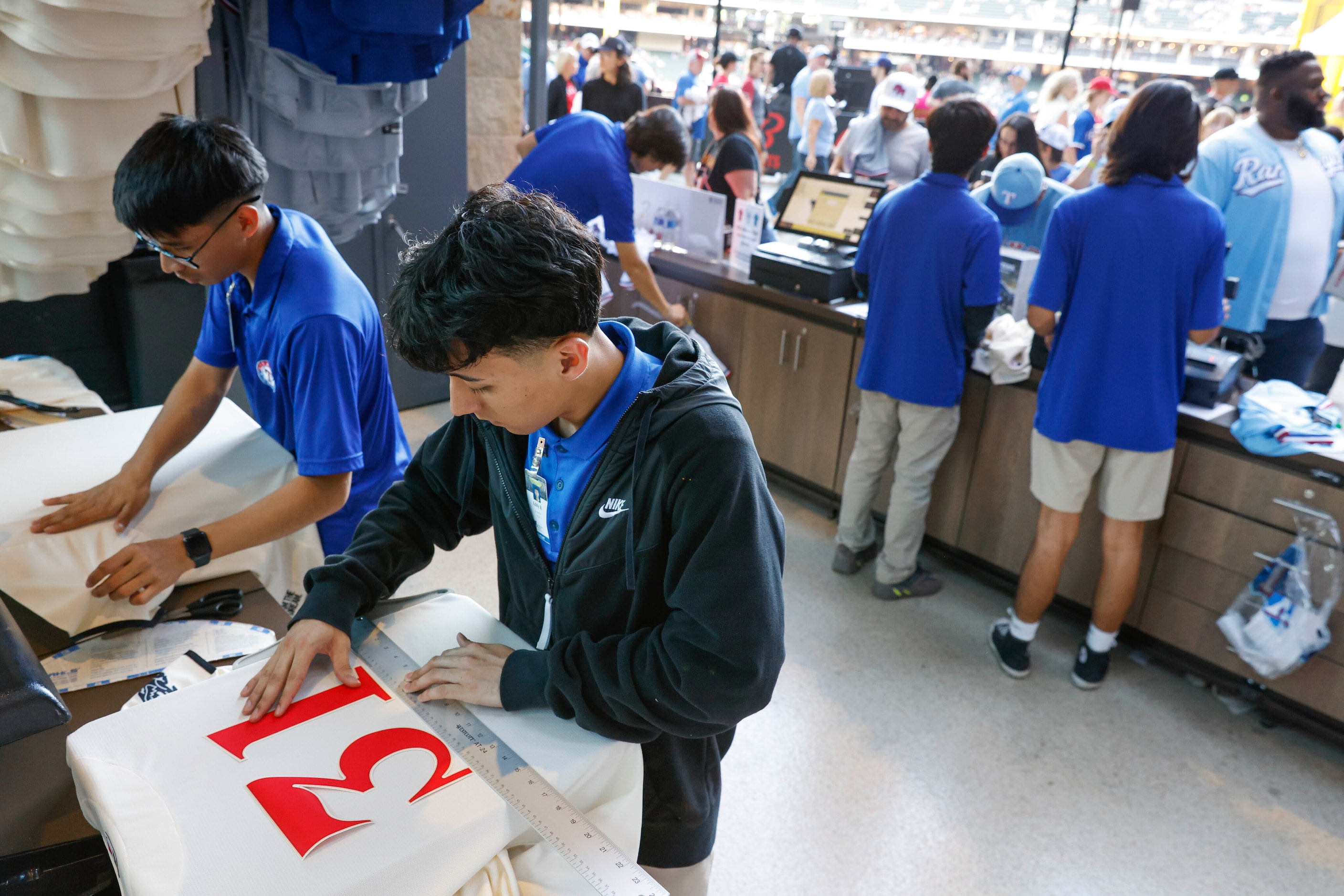 Eddy Briseno (center) prepares a Texas Rangers City Connect jersey for a customer before a...