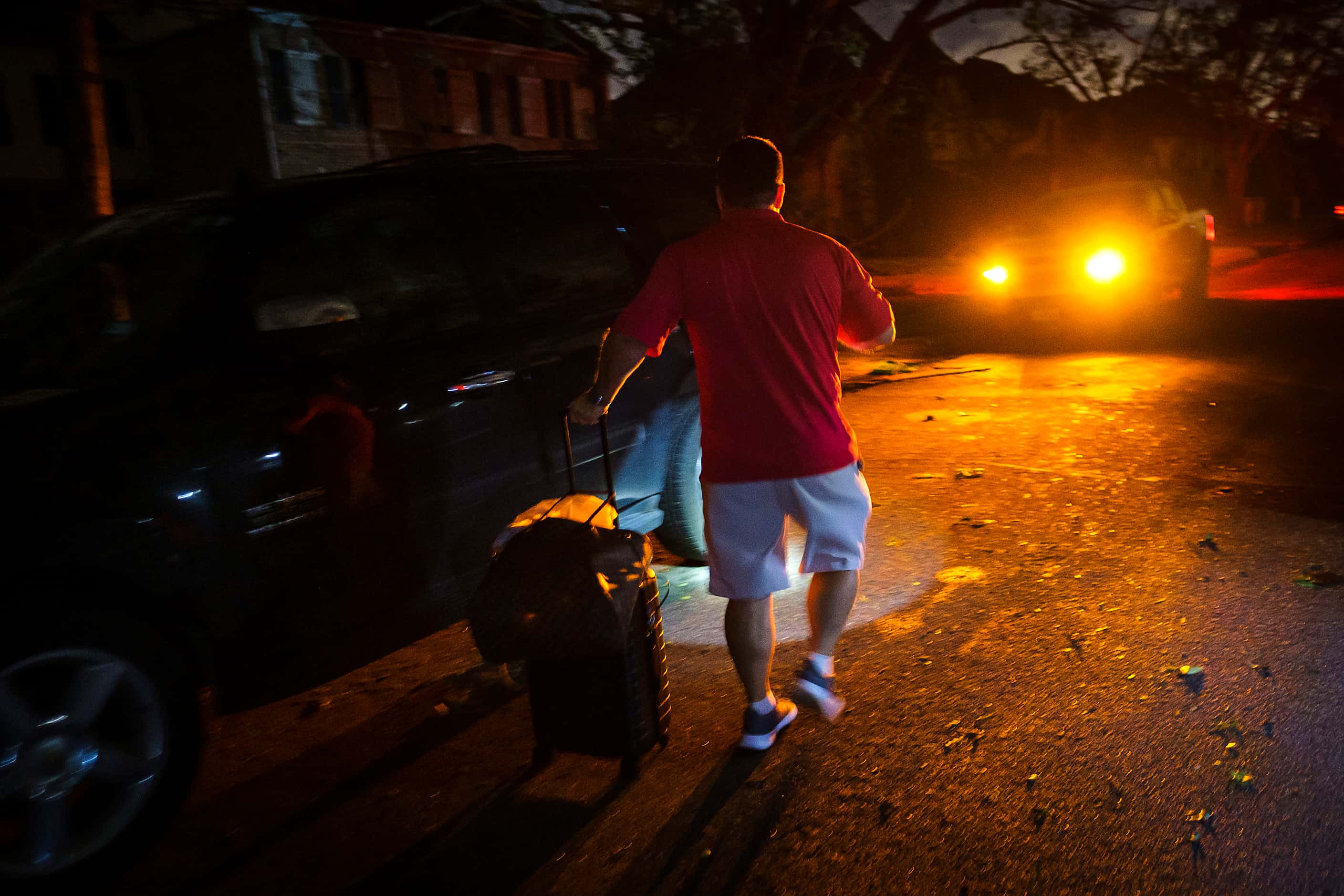 A resident takes a suitcase to his car in a darkened neighborhood near the intersection of...