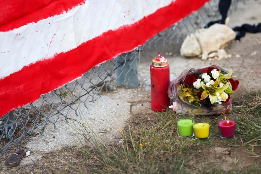 A candle burns near the first bouquet of flowers left at a mural along the fenceline of the...