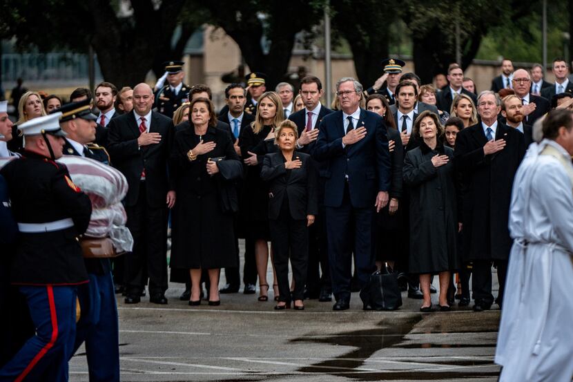 Friends and Bush family members salute and hold their hands over their hearts as they watch...