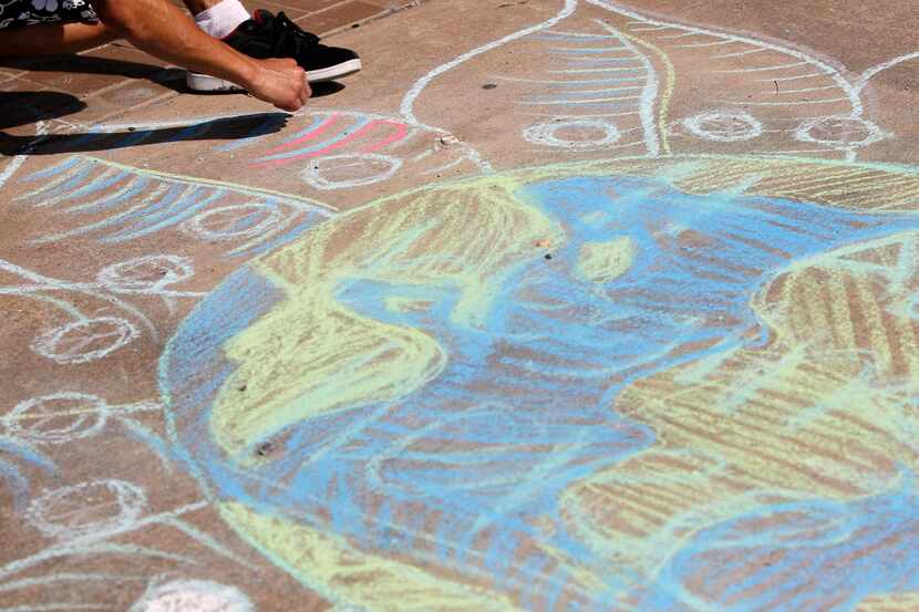 Kevin Sourivong uses sidewalk chalk to draw a picture of the Earth with flower petals...