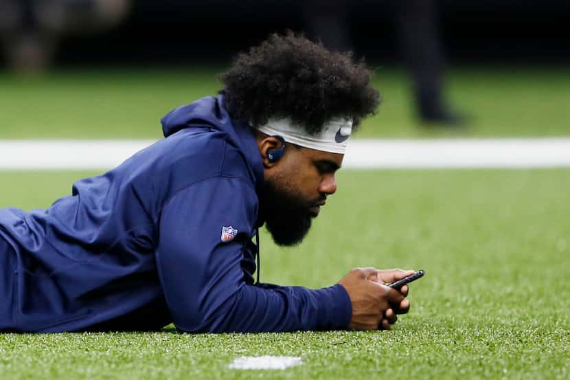 Dallas Cowboys running back Ezekiel Elliott (21) uses his phone on the field before a game...