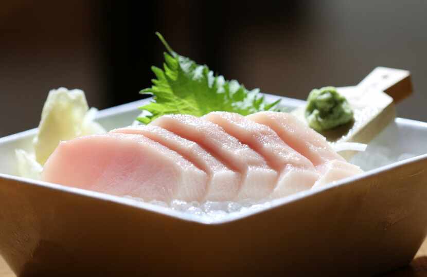 Hamachi sashimi garnished with wasabi (on the wooden paddle at right) and shiso (the leaf in...