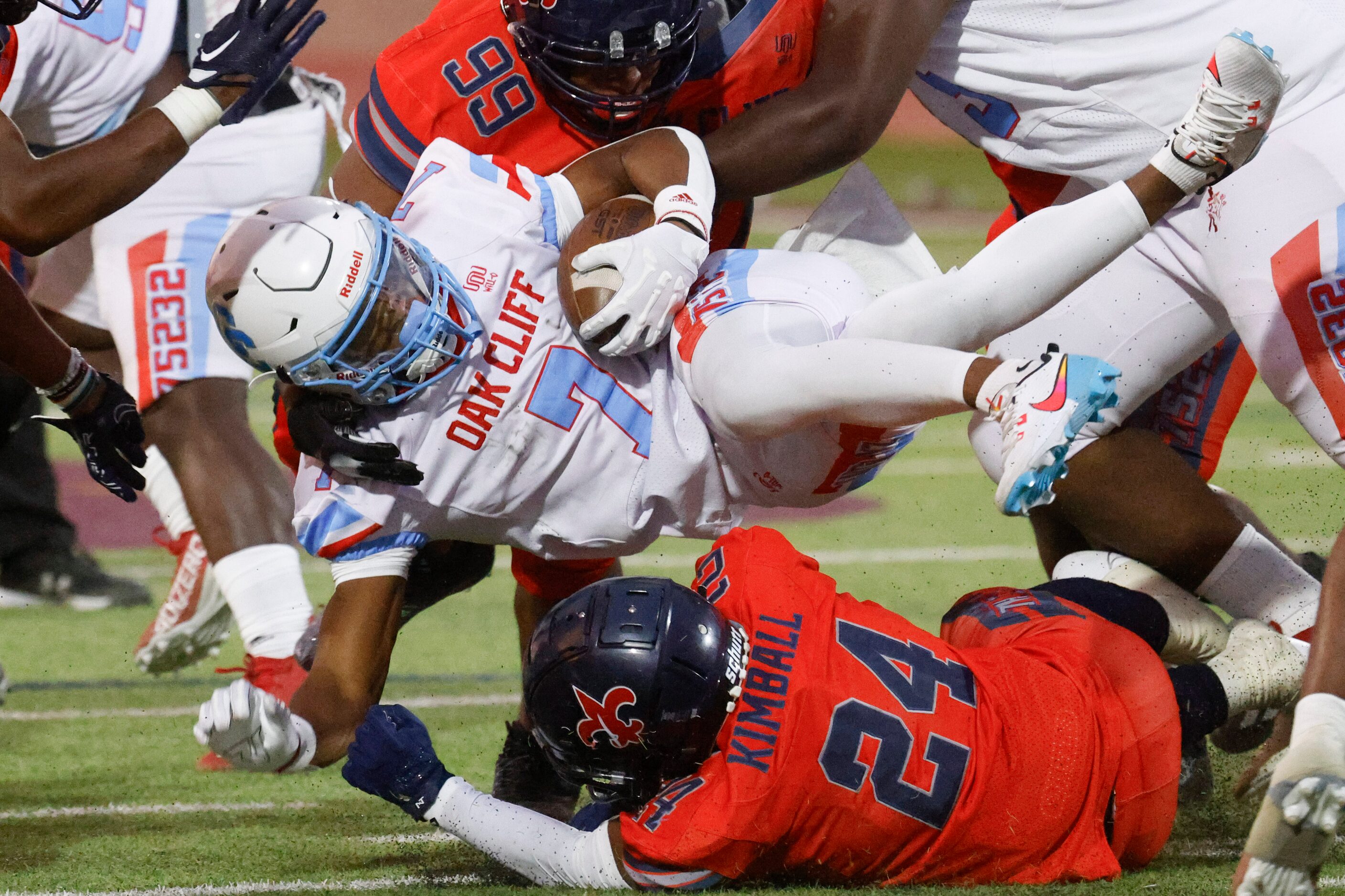 Carter High’s Kaeden Landry (center) gets charged by Kimball high’s Rodney Price (24) and...