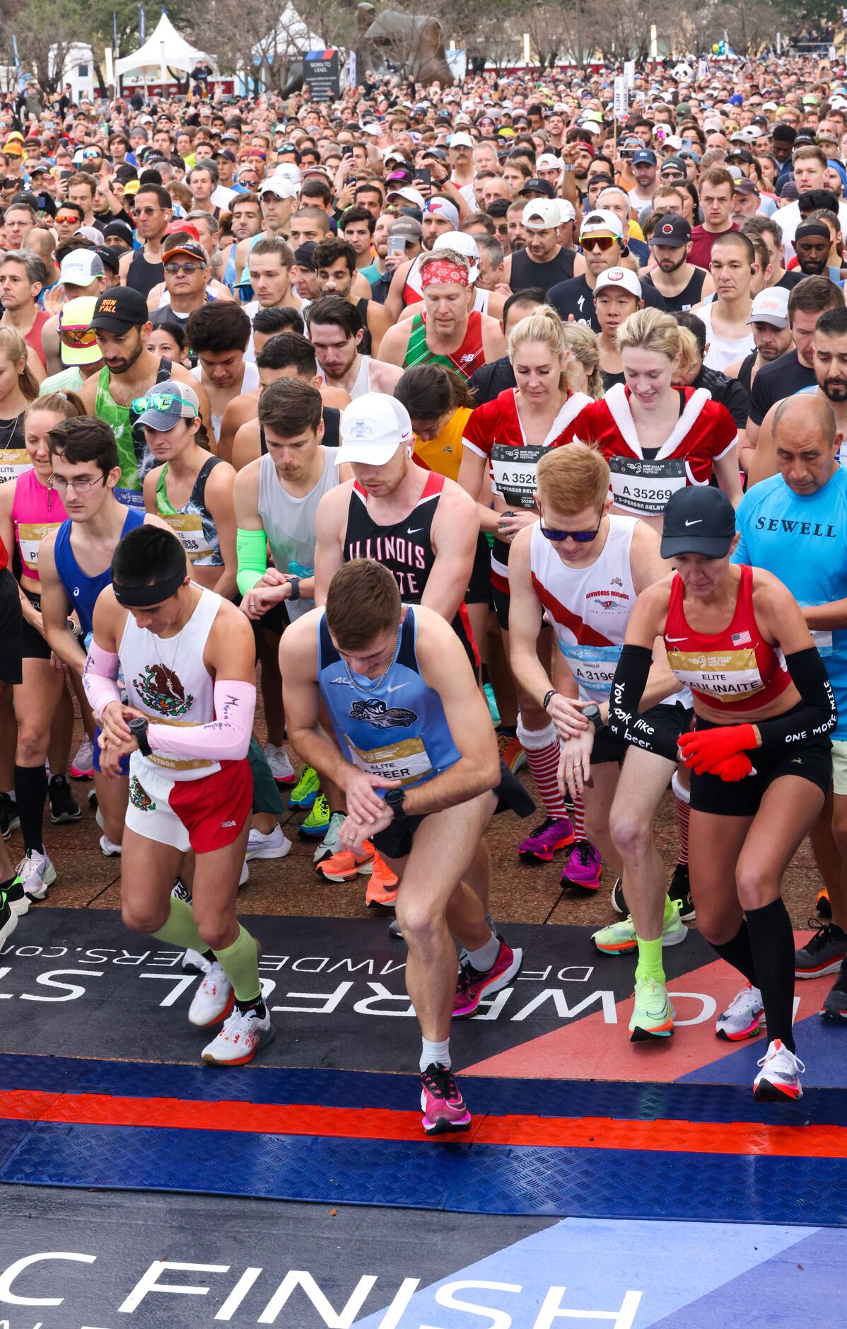 BMW Dallas Marathon runners start their watches as they cross the start line in front of...