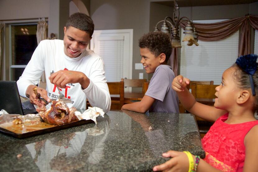 
Bishop Dunne senior quarterback Caleb Evans, 17, cuts off pieces of a baked chicken for his...