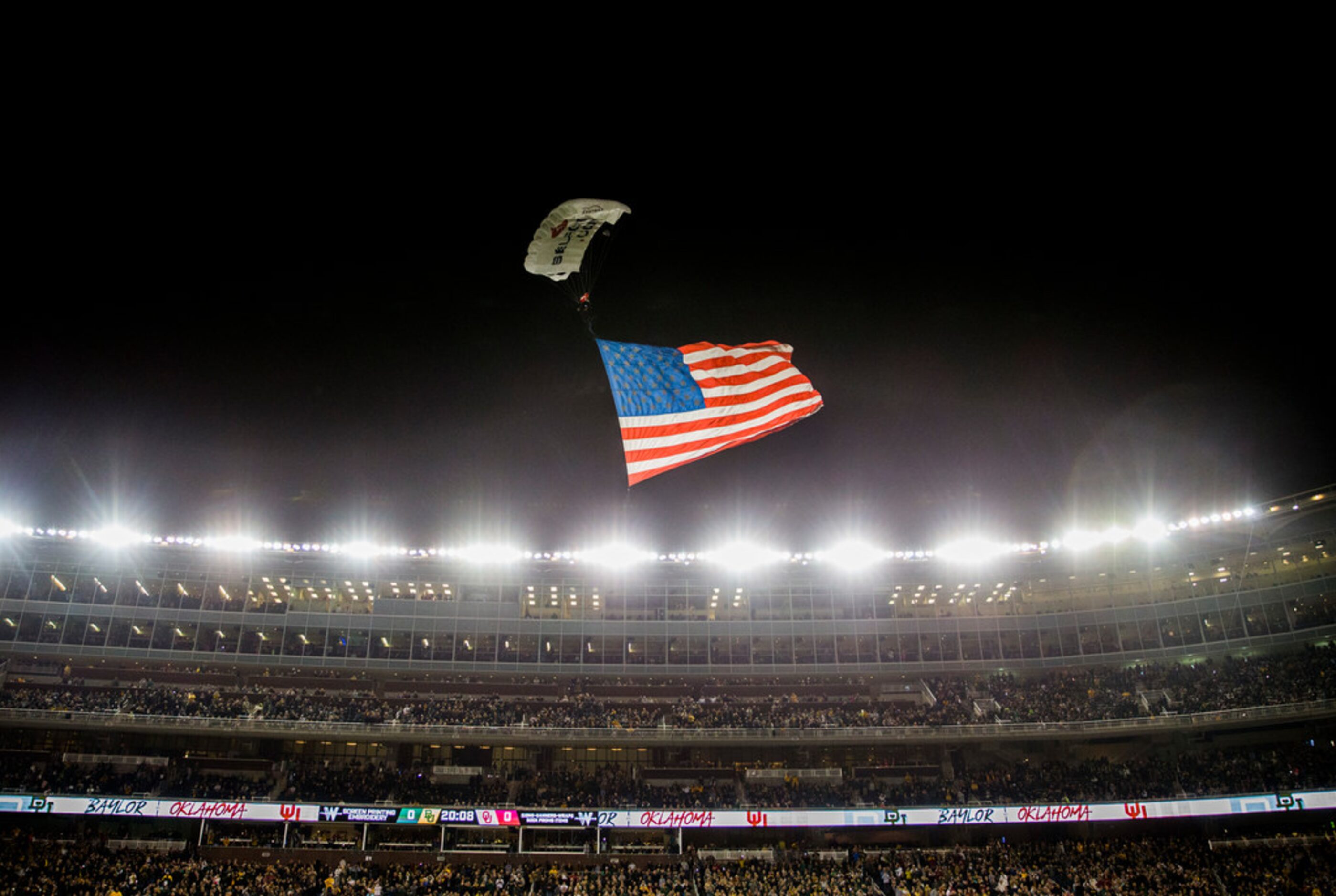 A parachuter lands on the field with an American flag before an NCAA football game between...