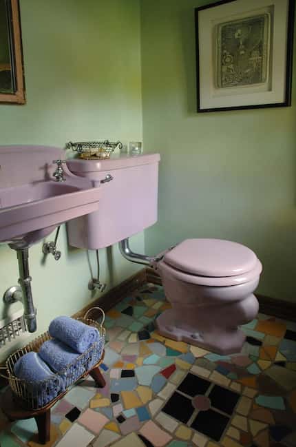 This bathroom has pale green walls, a multicolored mosaic floor and a pink toilet and pink...